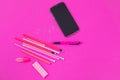 Pink office equipment and one black mobile phone are lying on pink background isolated