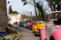 Pink old convertible car behind most of the other old, colorful cars