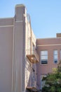 Pink or orange stucco building with fire escape ladder or escape balcony in sun with some shade on blue sky background Royalty Free Stock Photo