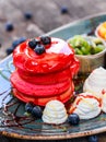 Pink pancakes with honey, chocolate, jam, whipped cream, berries and fruits on plate.