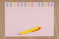 Pink paper sheet fixed with multi-colored paper clips on oak Board table close, yellow ballpoint pen, for background Royalty Free Stock Photo