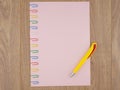 Pink paper sheet fixed with multi-colored paper clips on oak Board table close, yellow ballpoint pen