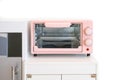 Pink pastel colour of Microwave, a modern kitchen appliance toys for kids to make up table settled in a white playroom