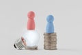 Pink pawns with light bulb and blue pawn on piles of coins - Concept of creativity and gender pay gap