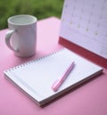 Pink pen on top of notebook with calendar and cup of coffee at the background Royalty Free Stock Photo
