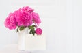 Pink peonies in white enamelled vase. Beautiful flowers in interior design. White paper for invitation text, white