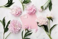 Pink peony flowers, envelope and paper card on white stone table top view in flat lay style.