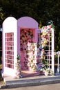 Pink phone booth decorated colourful flowers. Elegant wedding photo zone outdoor. Beautiful romantic festive place made with woode