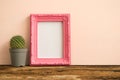 Pink photo frame on old wooden table with cactus over pink wall