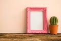 Pink photo frame on old wooden table with cactus over pink wall