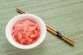 Pink pickled ginger in a white porcelain bowl and wooden chopsticks on a green wicker table mat. Traditional Japanese condiment Royalty Free Stock Photo