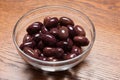 Pink pickled olives in a glass bowl, on a wooden table, closeup Royalty Free Stock Photo