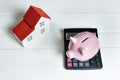 Pink pig piggy bank, calculator and breadboard model of a house with a red roof on a light background. Concept of renting, buying Royalty Free Stock Photo