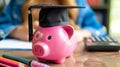Pink piggy bank with black graduation hat, book and calculator on the table. Savings for investment in education and Royalty Free Stock Photo