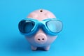 Pink piggy bank with blue swimming goggles on blue background like swimmer Royalty Free Stock Photo