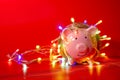 Pink piggy bank with Christmas string lights on happy December festival in Red background, Enjoy savings for spending money on the Royalty Free Stock Photo