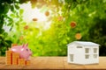 Pink piggy bank,coin dropping from top,stack gold dollar coin,on wood table,with house model,blurred nature background,concept