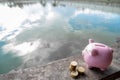 Pink piggy bank and gold coin pile on brown wooden with water and clouds background, step up growing business to success and Royalty Free Stock Photo