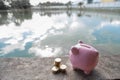 Pink piggy bank and gold coin pile on brown wooden with water and clouds background, step up growing business to success and Royalty Free Stock Photo