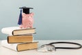 Pink piggy bank with graduation cap on stack of books and stethoscope. Concept of the costs of medical education Royalty Free Stock Photo