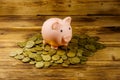 Pink piggy bank on a heap of coins on wooden background. Saving money concept Royalty Free Stock Photo