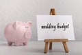 Pink piggy bank with note on easel and wedding word