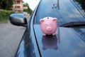 Pink piggy bank standing on the black car, saving money for new car or saving money with car insurance