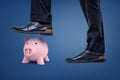 A pink piggy bank stands under a dangerous male foot which is ready to step on it.