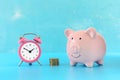 Pink piggy bank on a turquoise background. Next to a stack of coins and a small pink alarm clock. Bright picture. Royalty Free Stock Photo