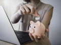 Pink piggy bank in woman`s hand and she put a blank silver money coin into it.