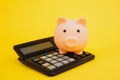 Pink piggy or coin bank or piggybank or money box on calculator - finance and savings concept on yellow background Royalty Free Stock Photo