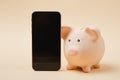 Pink piggy money bank mobile phone with blank empty screen on beige wall background. Money accumulation Royalty Free Stock Photo