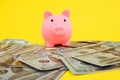 Pink piggy money box on dollar and euro banknotes on yellow background. Money saving concept