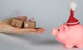 Pink piglet in a Santa Claus hat and human hand with Christmas presents in front of it Royalty Free Stock Photo