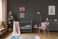 Pink pillow on grey armchair next to kid`s bed with blanket in b