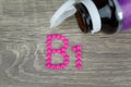 Pink pills forming shape to B1 alphabet on wood background