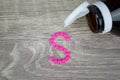 Pink pills forming shape to S alphabet on wood background Royalty Free Stock Photo