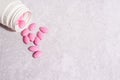 Pink pills pouring out of the white bottle on light concrete background, medicine Royalty Free Stock Photo