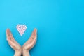 Pink pills in the shape of a heart on a blue background and female hands surround a heart made of pills