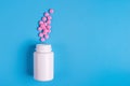 Pink pills, tablets and white bottle on blue background