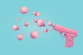 Pink pistol shooting Christmas ball bauble ornaments instead of bullets on pastel blue background