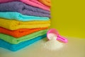 Pink plastic measuring vessel with washing powder, containers with detergent, stack terry towels