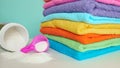 Pink plastic measuring vessel with washing powder, containers with detergent, stack terry towels