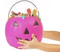 Pink plastic pumpkin filled with candy, hand of kid