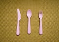 Pink, plastic spoon, fork, knife lie on brown background Royalty Free Stock Photo