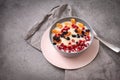 plate of oatmeal porridge with fruit slices, tangerine slices, raisins, dried apricots, pomegranate seeds on a gray background,