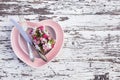 Pink plate in the shape of a heart with silver knife and fork and decorative flowers on white wooden background. Top view. Love Royalty Free Stock Photo