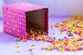 A pink polka dot gift box, multi-colored beads scattered on a table. Festive fun