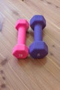 Pink and purple exercise hand weights side by side on a light wood background, copy space