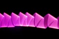 Pink and purple shining neon wave of light as curls or swirl with smooth stripes on black background.